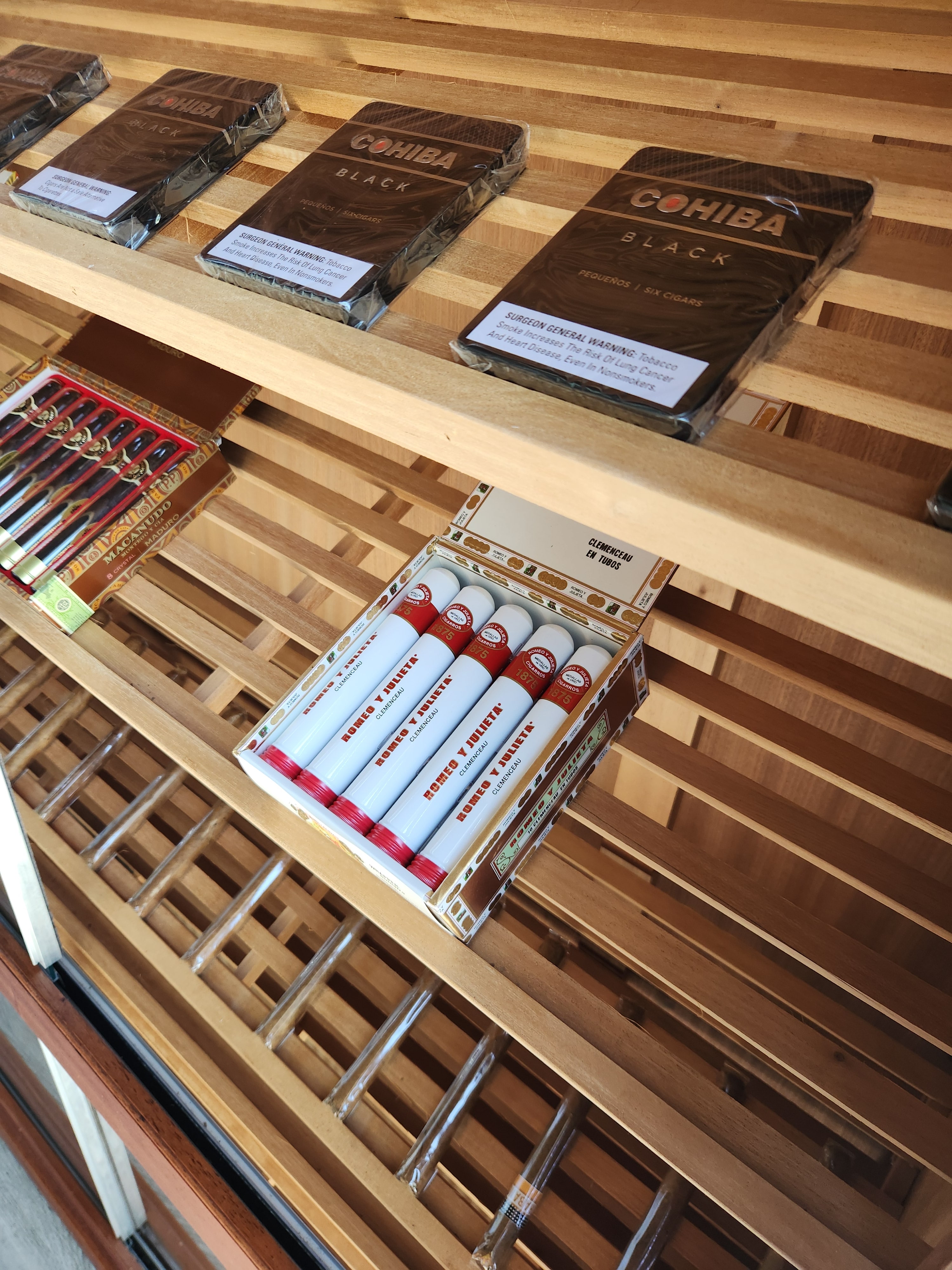 Boxes of Cohiba Black Pequenos on the cedar shelves beside an open box of Romeo y Julieta 1875 Clemenceau tubos.