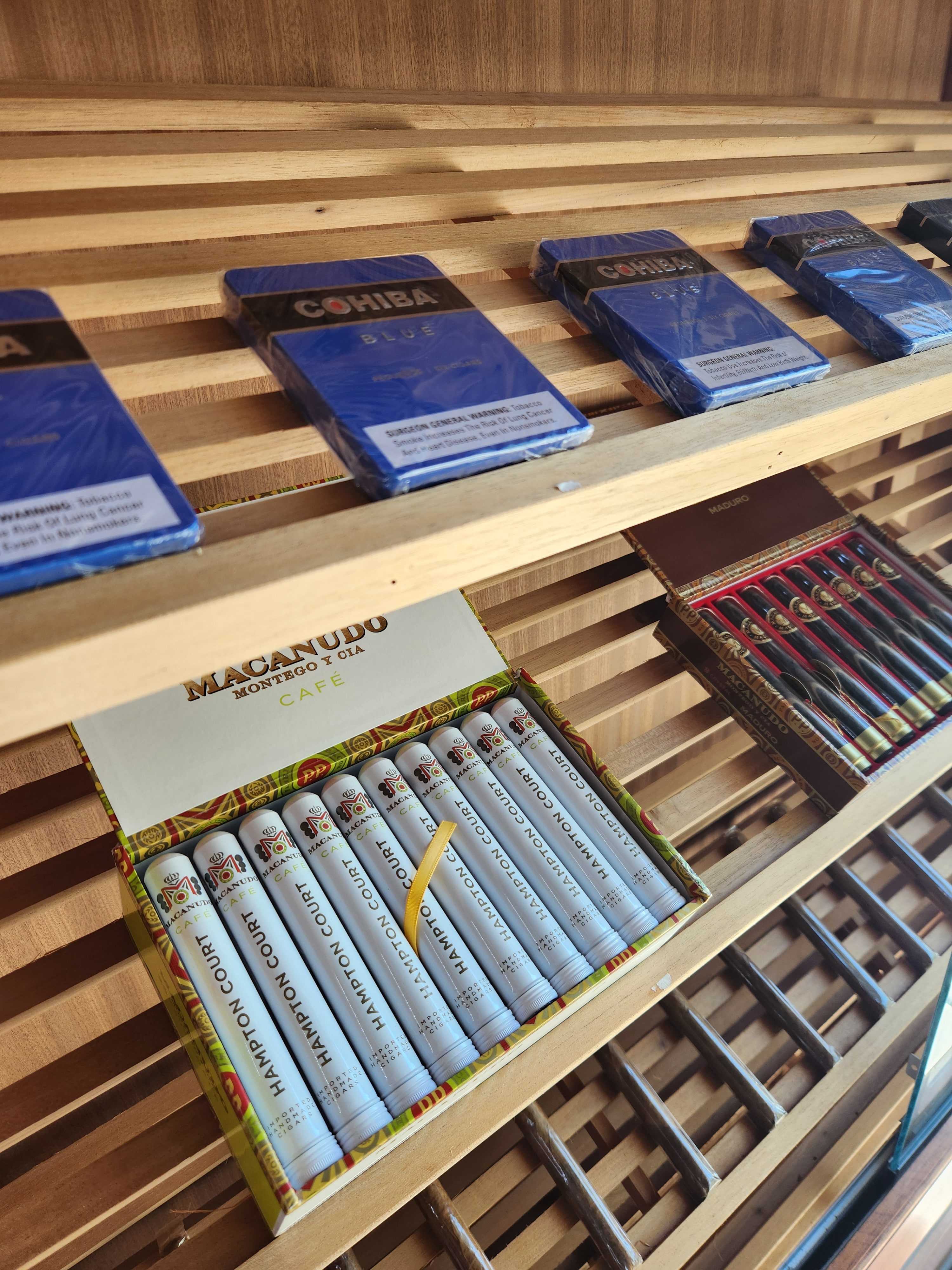 Cohiba Blue boxes on the humidor shelf next to an open box of Macanudo Cafe Hampton Court tubes.
