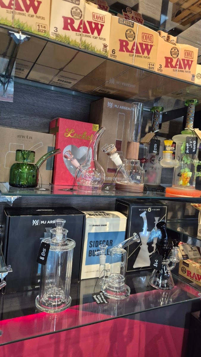 Rolling papers and cones on a shelf beside glass pieces.