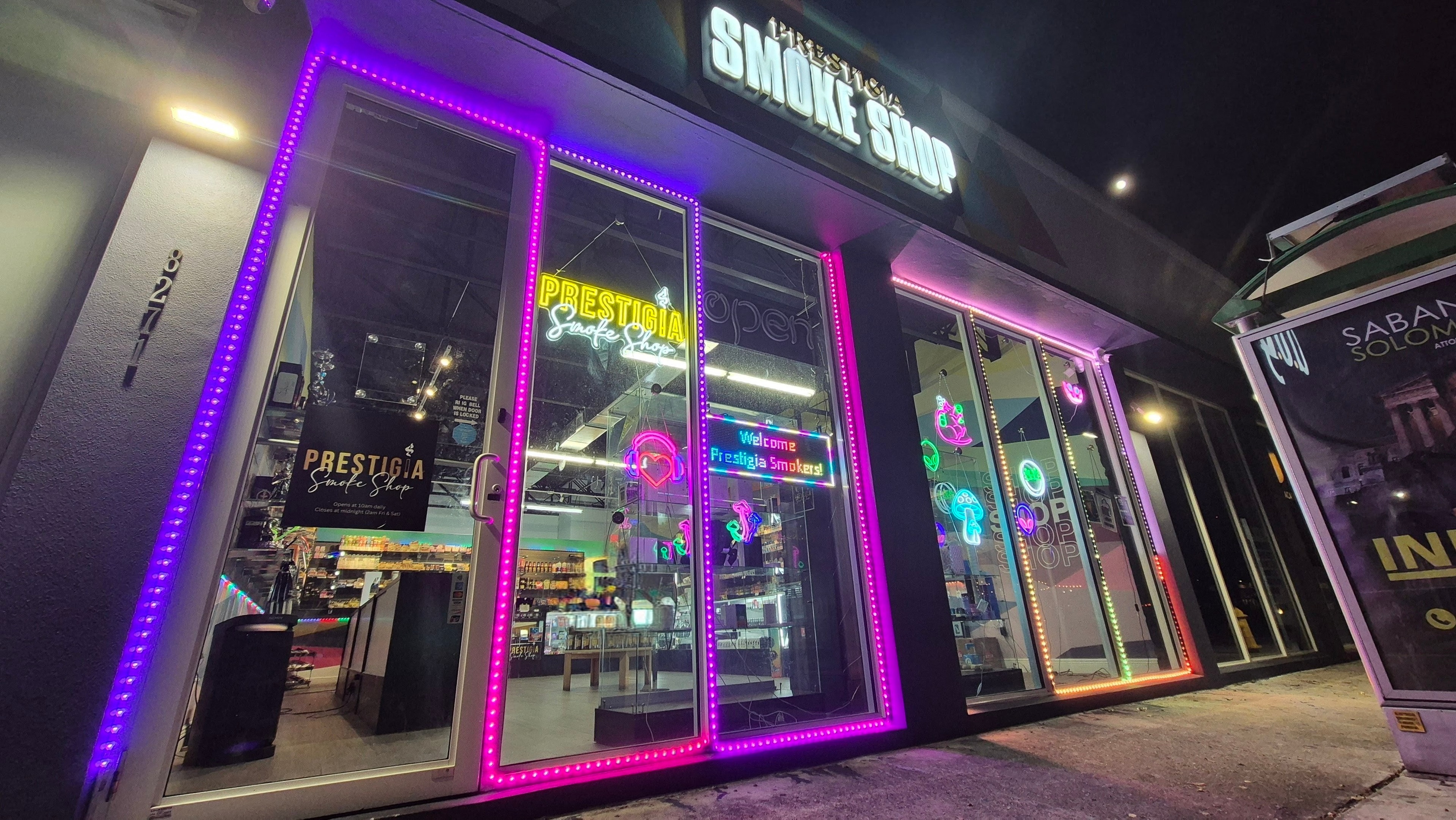 Prestigia Smoke Shop at night, its backlit storefront sign lit above LED-framed windows on NE 2nd Avenue.
